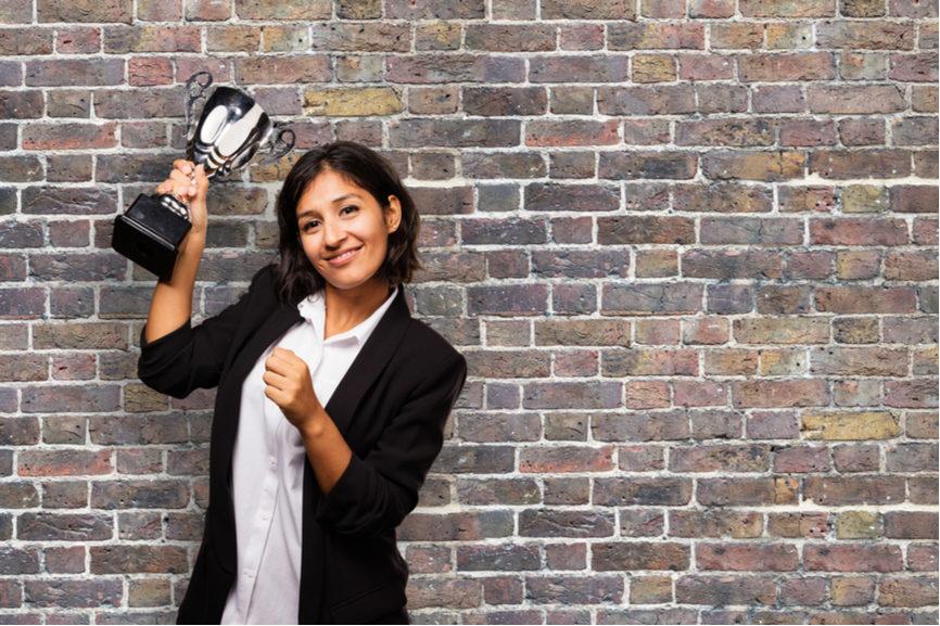 woman holds award in front of brick wall