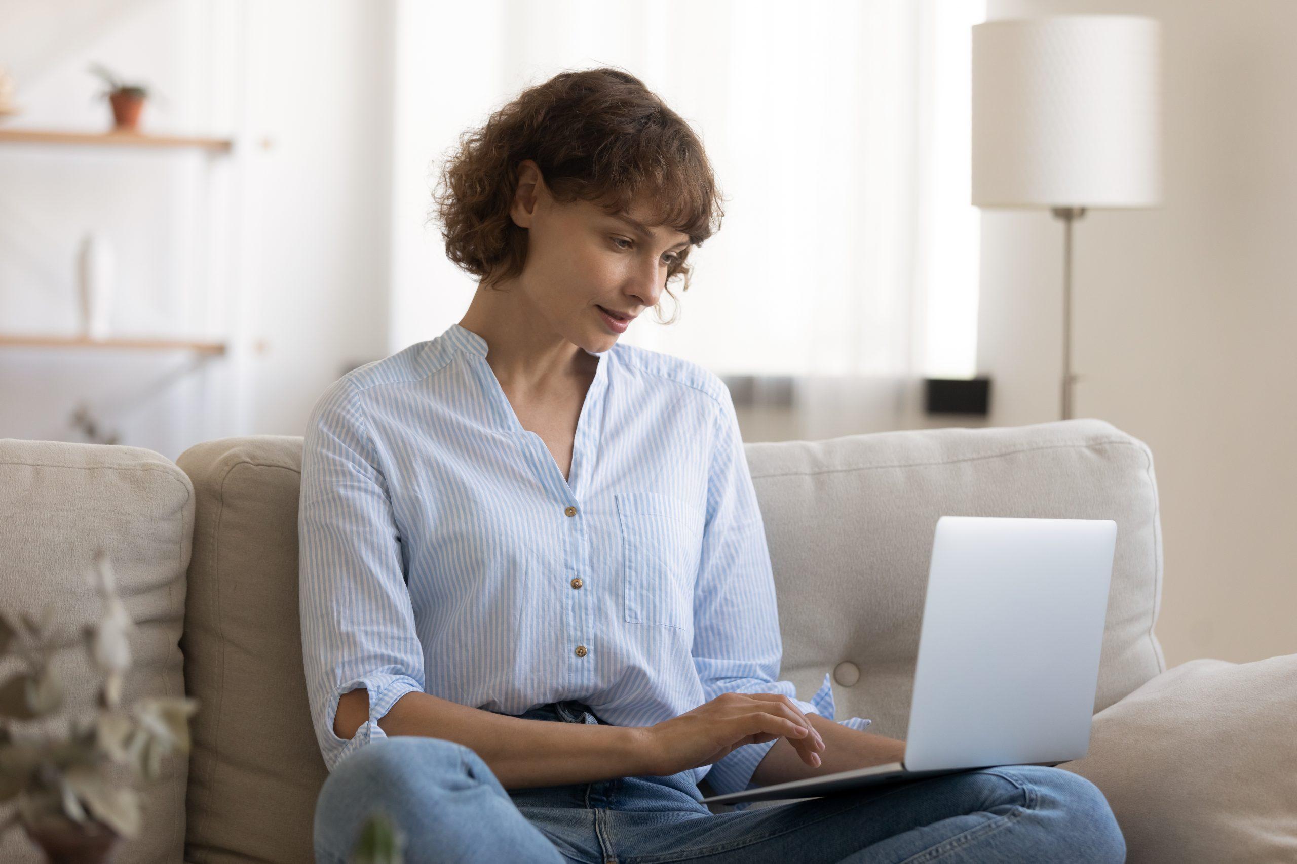 woman sitting on couch writing on a laptop computer