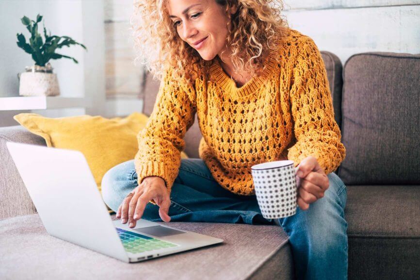 Woman sitting on a couch and looking at a laptop while drinking coffee