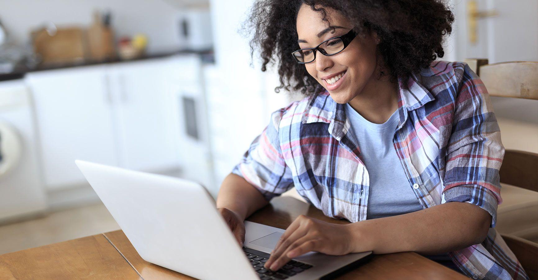 Happy young woman working on a laptop at a kitchen table