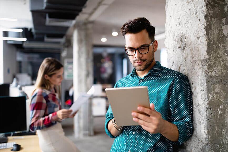 Man looking at tablet while woman behind him is looking at document