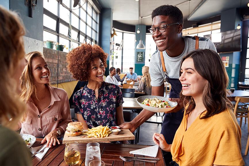 Waiter happily serving a group of people their food at a restaurant