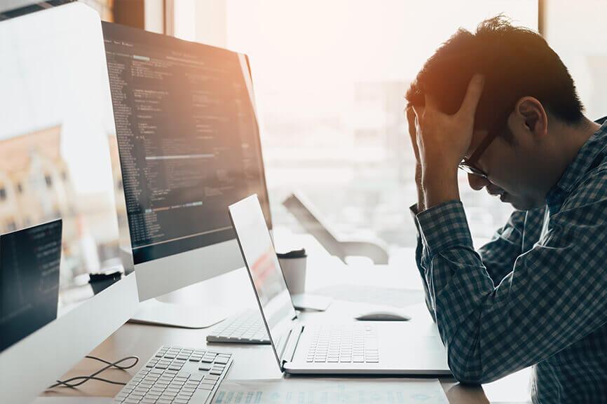 Man with his head in his hands looking frustrated in front of computers