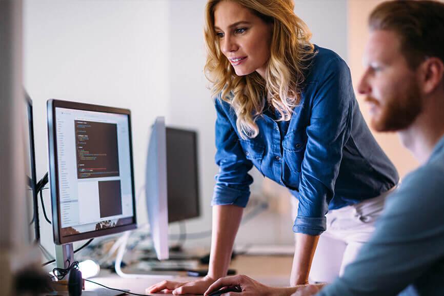 Woman looking over at her coworker's desk to look at his desktop screen