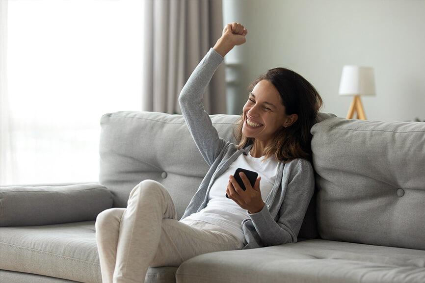 Woman on a couch with her fist in the air while holding phone