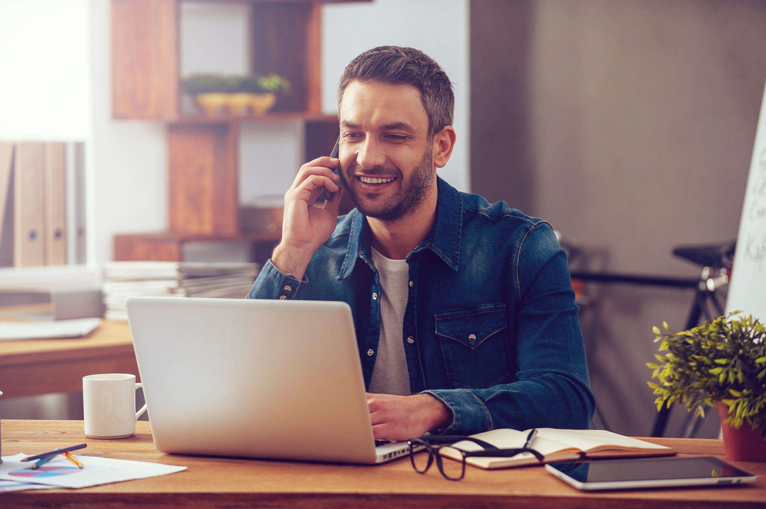 Happy Man Answering Phone While Using Laptop 1