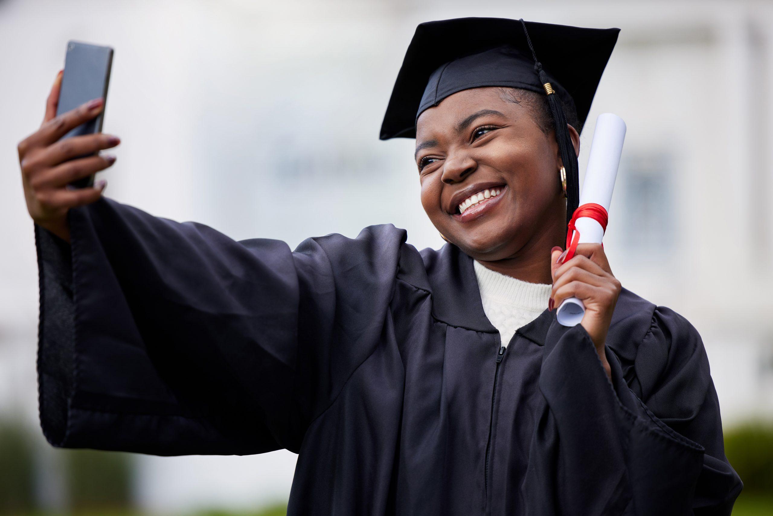 graduate with cap and gown taking selfie excited