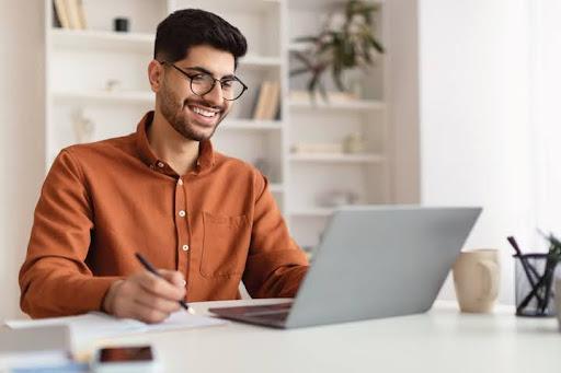 Man uses computer and writes with pen