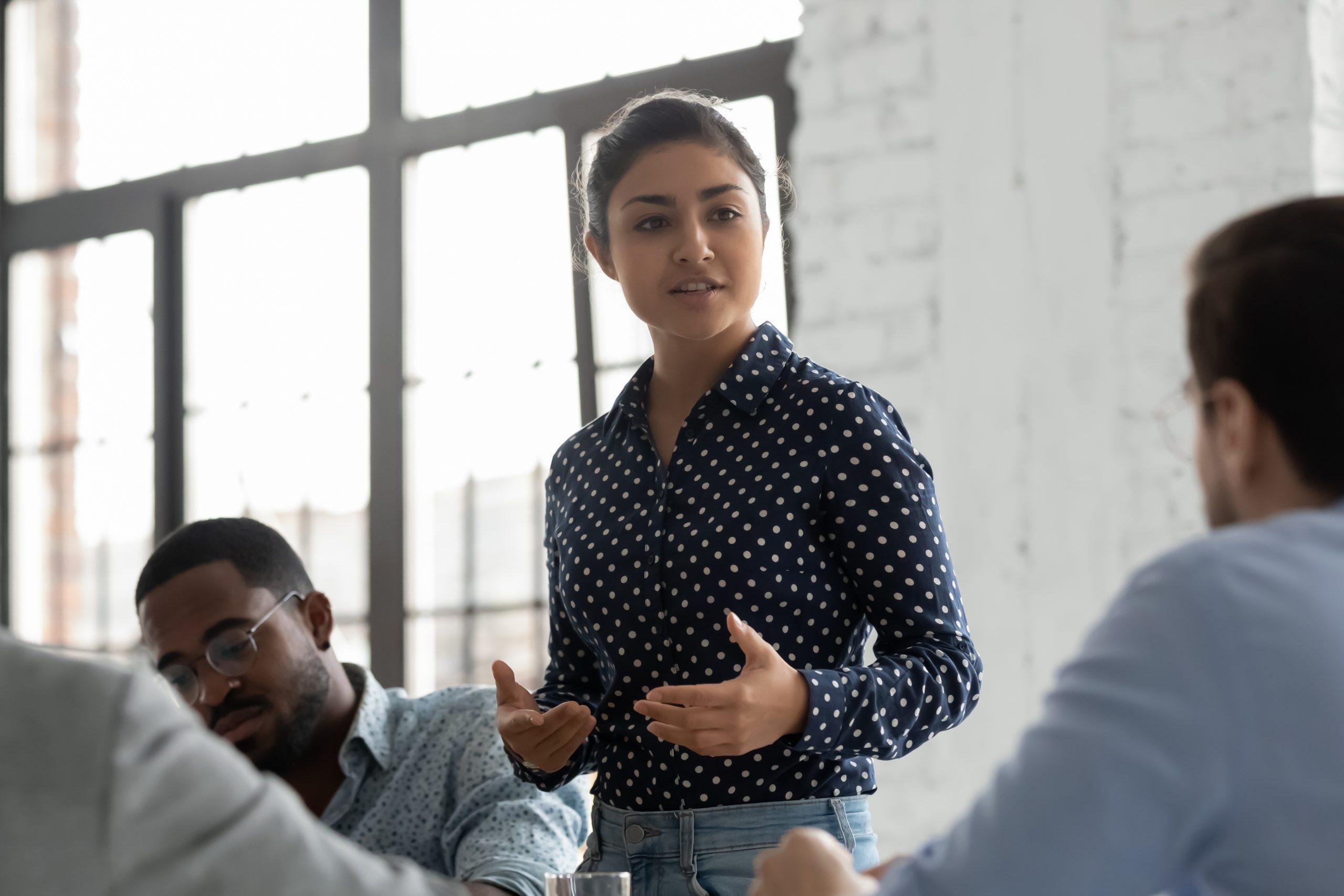 woman speaking while standing up in front of coworkers meeting