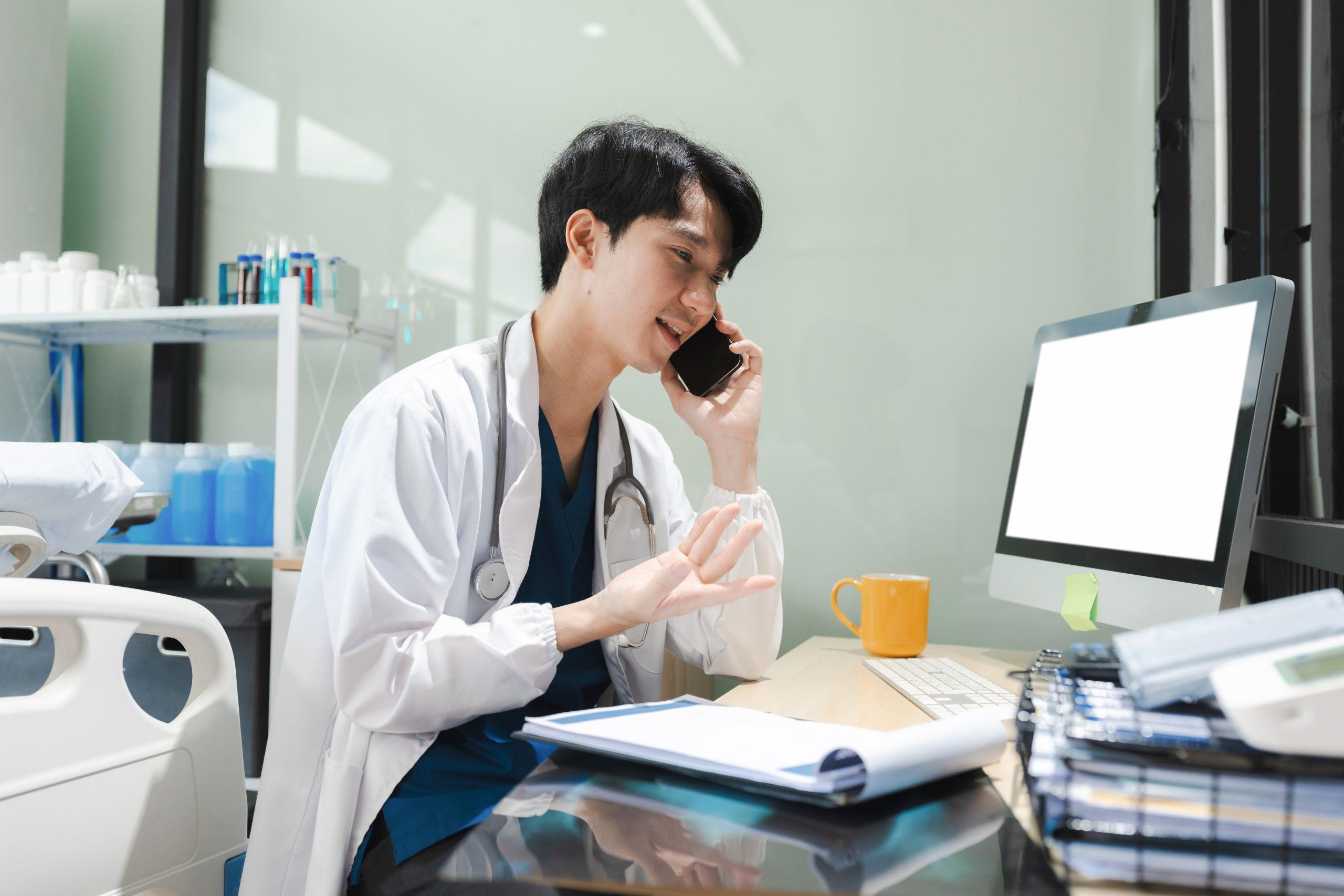 physician speaking on the phone while sitting at his desk in a medical office